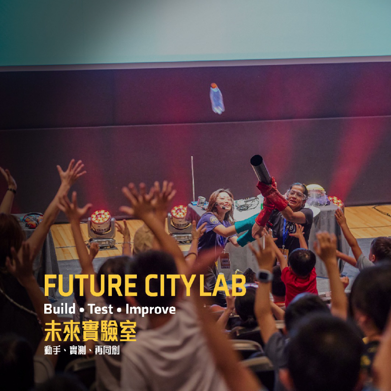 Children raise their hands as the facilitator demonstrates a science experiment with a launcher.