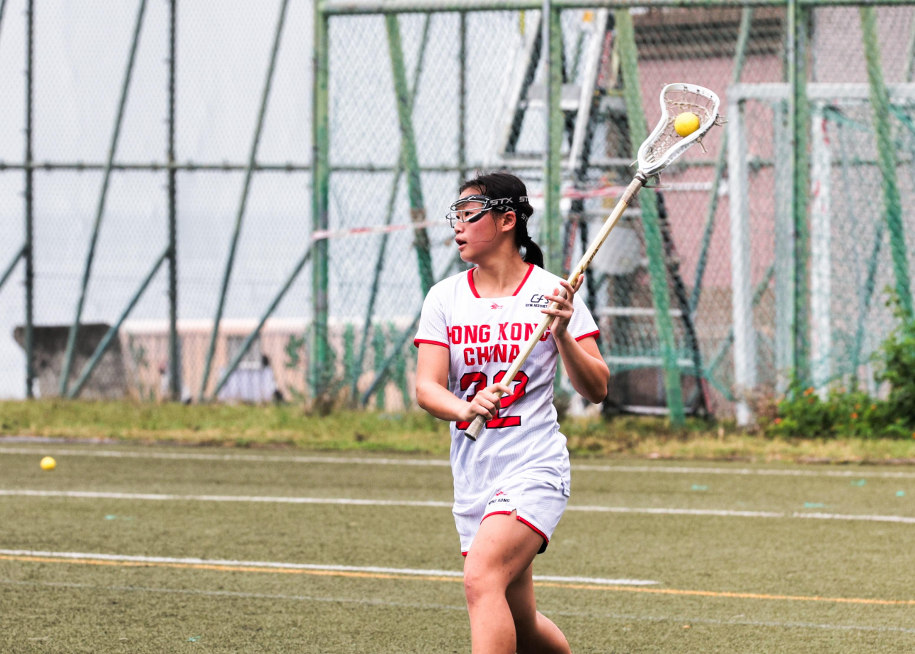 The Hong Kong Jockey Club Compassionate Leader Scholarship awardee, Samantha Yeung holds a lacrosse stick on a field.