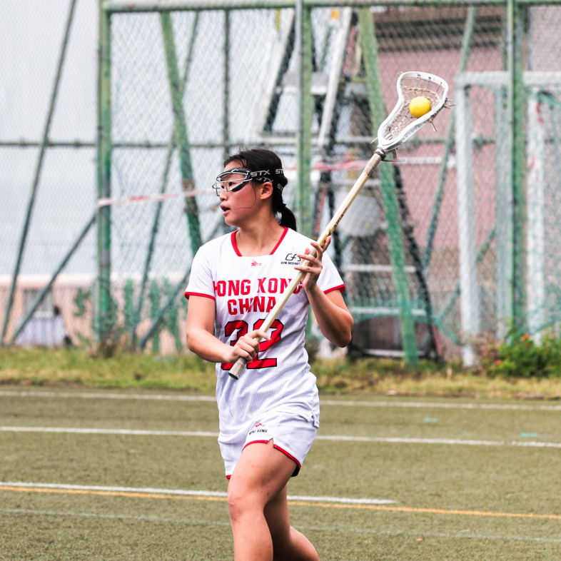 The Hong Kong Jockey Club Compassionate Leader Scholarship awardee, Samantha Yeung holds a lacrosse stick on a field.
